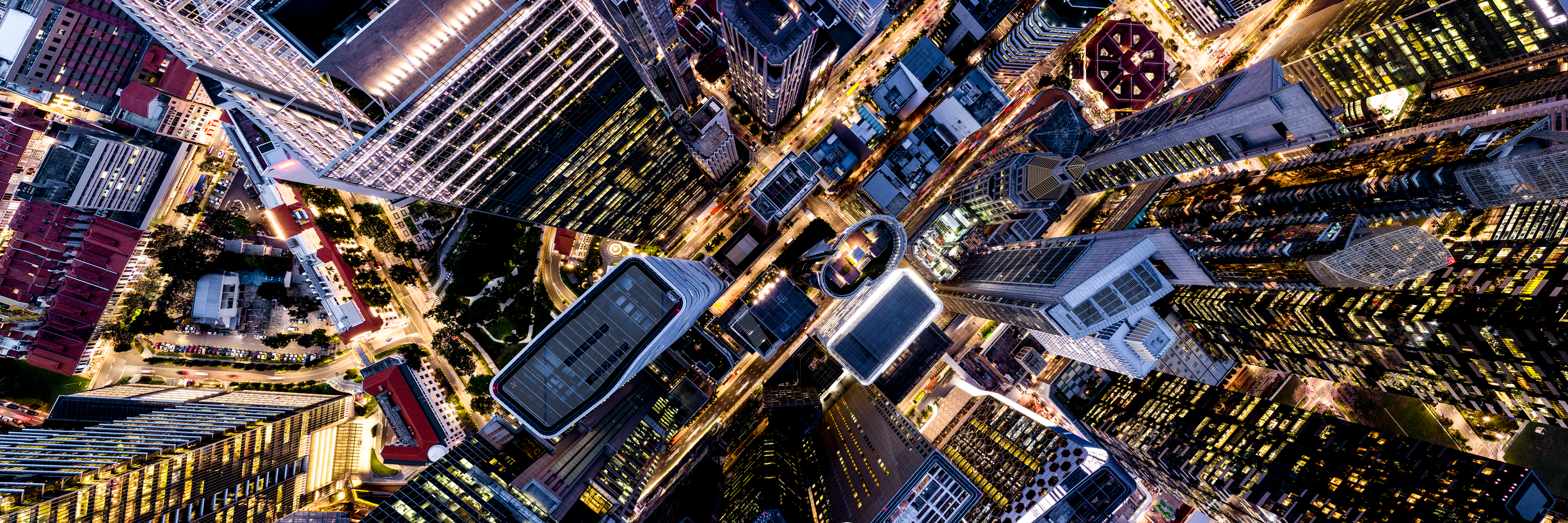 A top-down aerial view of a dense urban cityscape at night, with illuminated skyscrapers, grid-like streets, and glowing windows creating a complex geometric pattern. The image captures the vibrant energy and architectural density of a modern metropolis.
